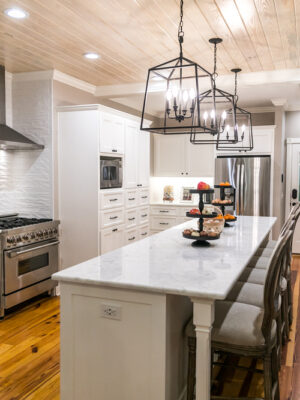 Large renovated white kitchen with updated cabinets, textured subway tile, black iron lights and pine hardwood flooring.