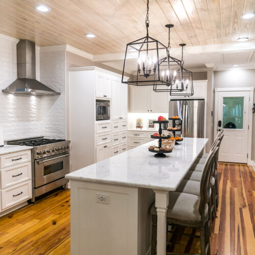 Large renovated white kitchen with updated cabinets, textured subway tile, black iron lights and pine hardwood flooring.